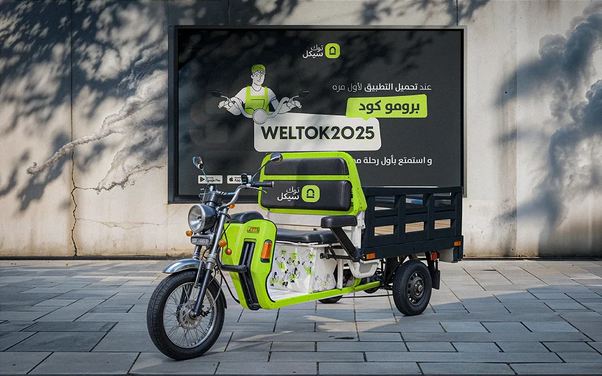A lime and navy Tukcycle cargo tricycle parked under a campaign poster